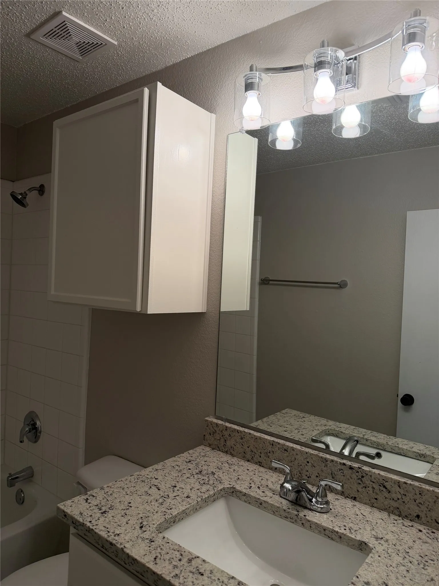 Bathroom featuring a polished chrome light fixture, vanity mirror, granite-finish countertop, under-mount sink, and built-in storage cabinet