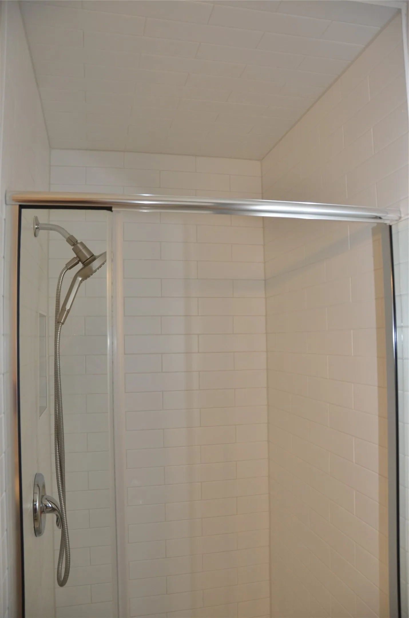 Shower enclosure with clear glass sliding door, subway tile walls, a handheld shower fixture, and chrome finishes