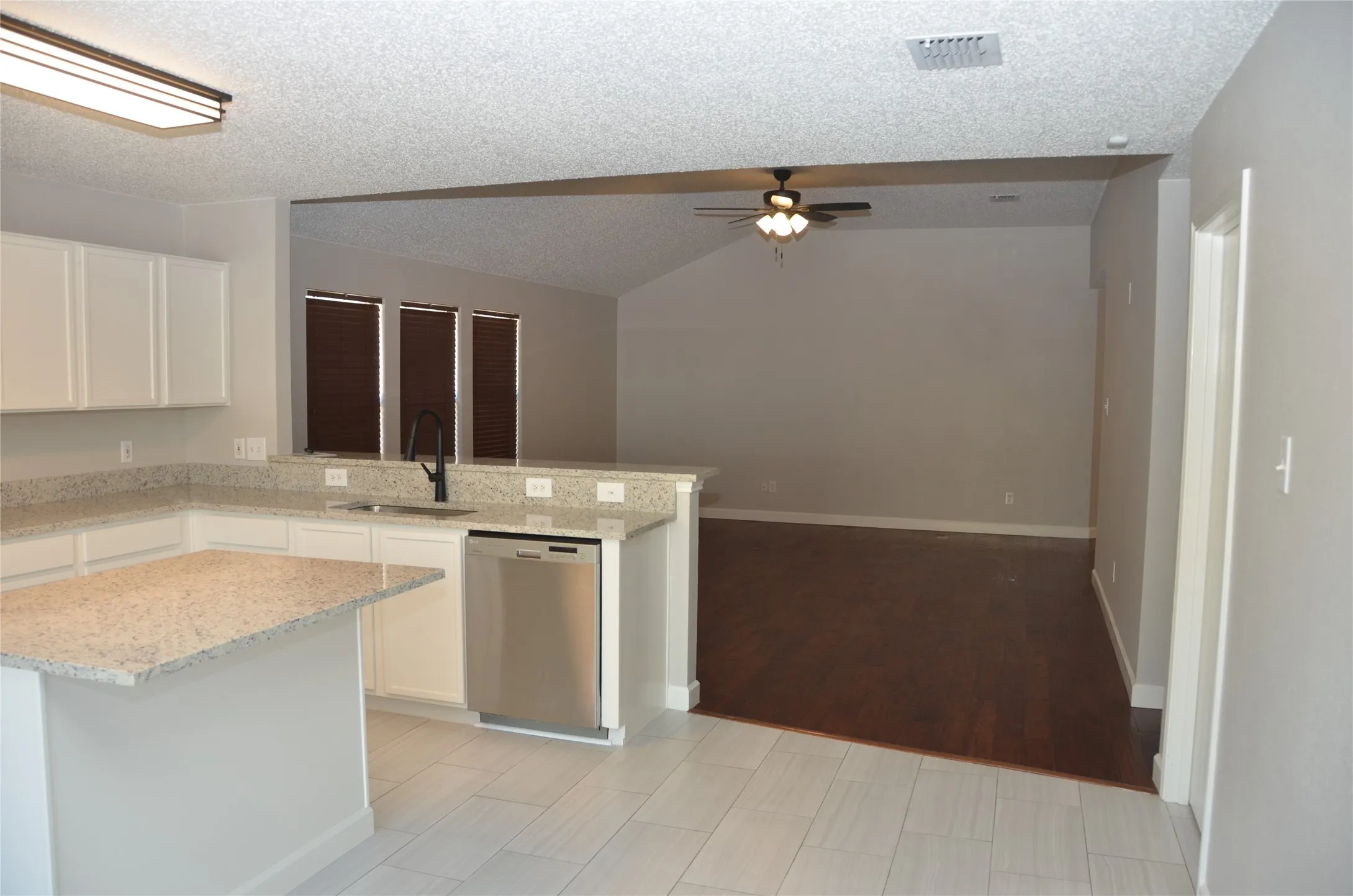 Kitchen featuring white cabinetry, light-toned countertops, stainless steel dishwasher, and a black faucet
