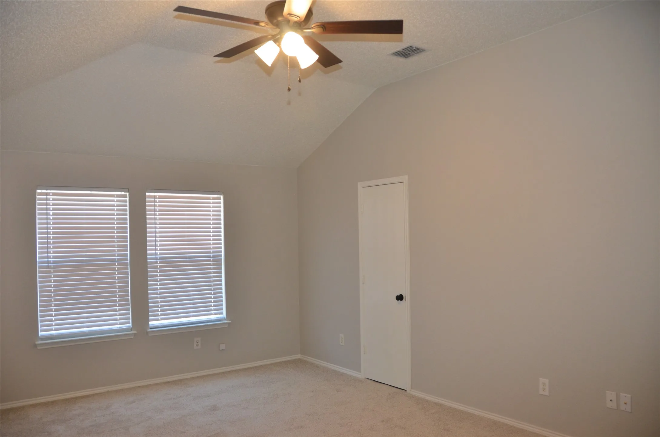Vaulted ceiling with a ceiling fan light fixture, two windows with horizontal blinds, neutral wall paint, and carpet flooring
