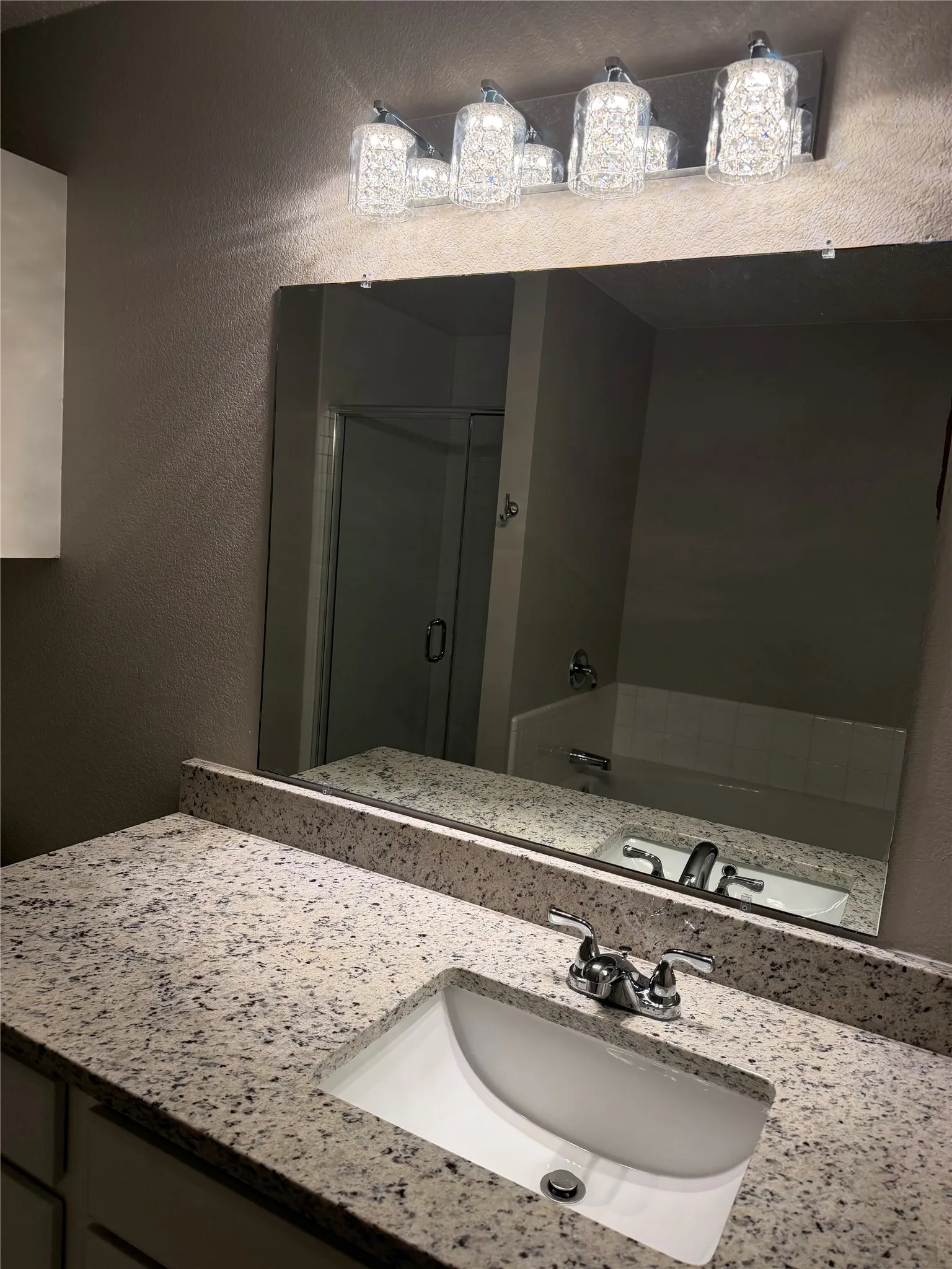 Vanity with speckled countertop, undermount sink, chrome faucet, and decorative light fixture