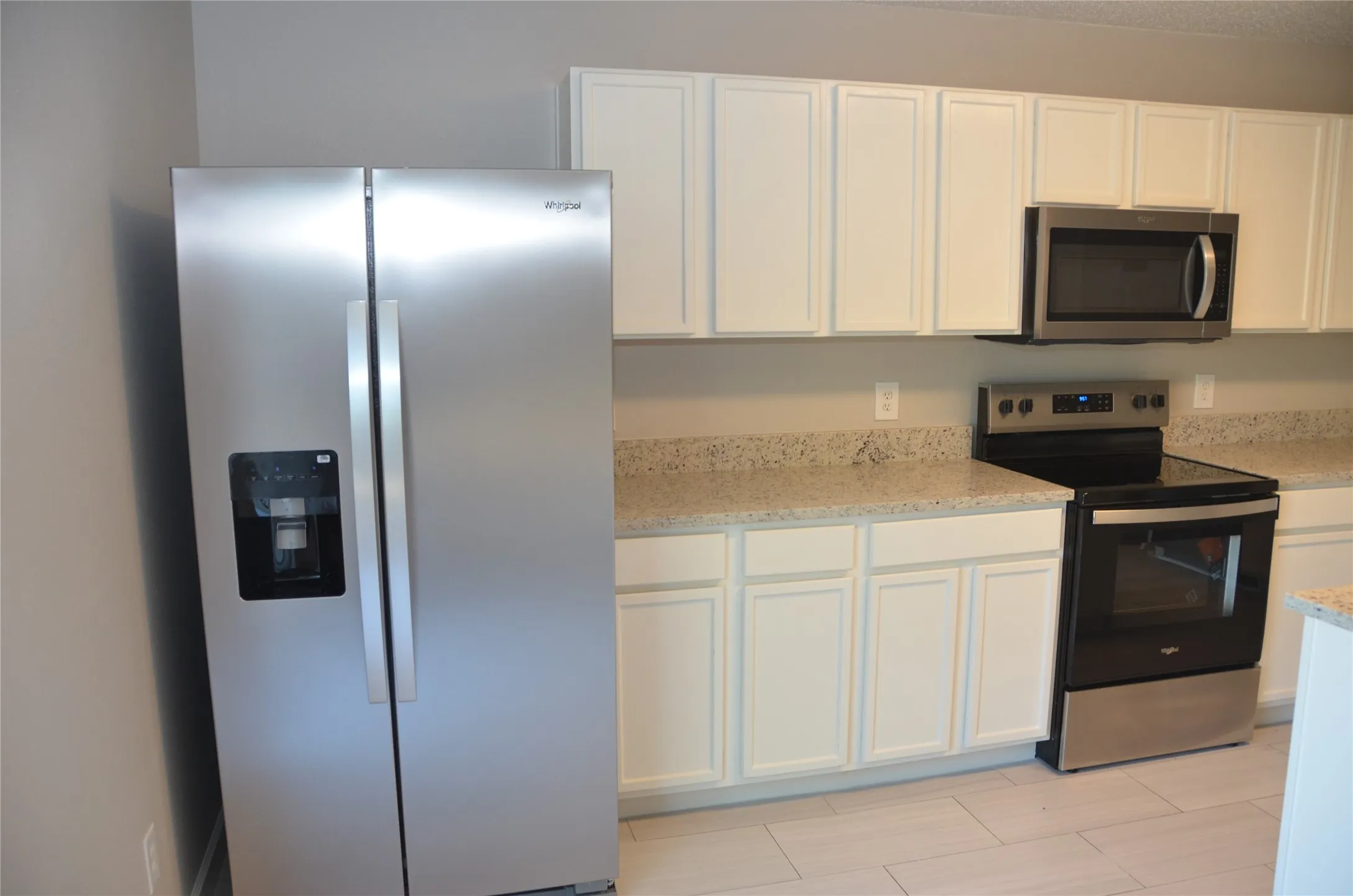 Stainless steel side-by-side refrigerator, white upper and lower cabinetry, speckled countertops, stainless steel and black range, and an over-the-range microwave