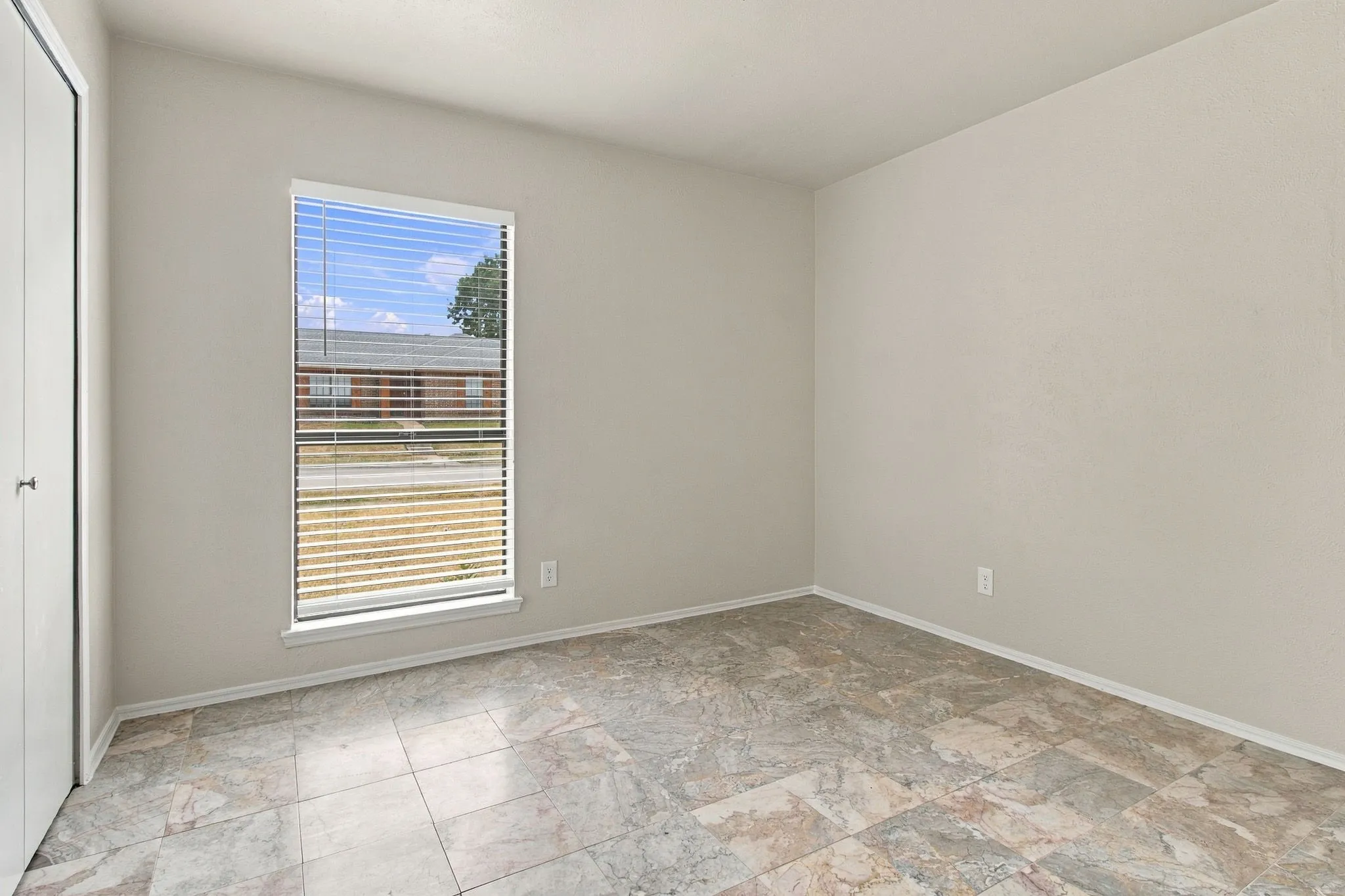 Recessed window with blinds, light-toned walls, and multi-toned tile flooring