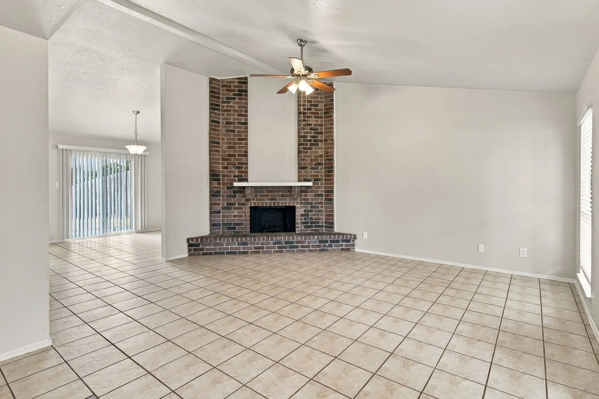 Spacious interior featuring tile flooring, a brick fireplace with a mantel, and a ceiling fan