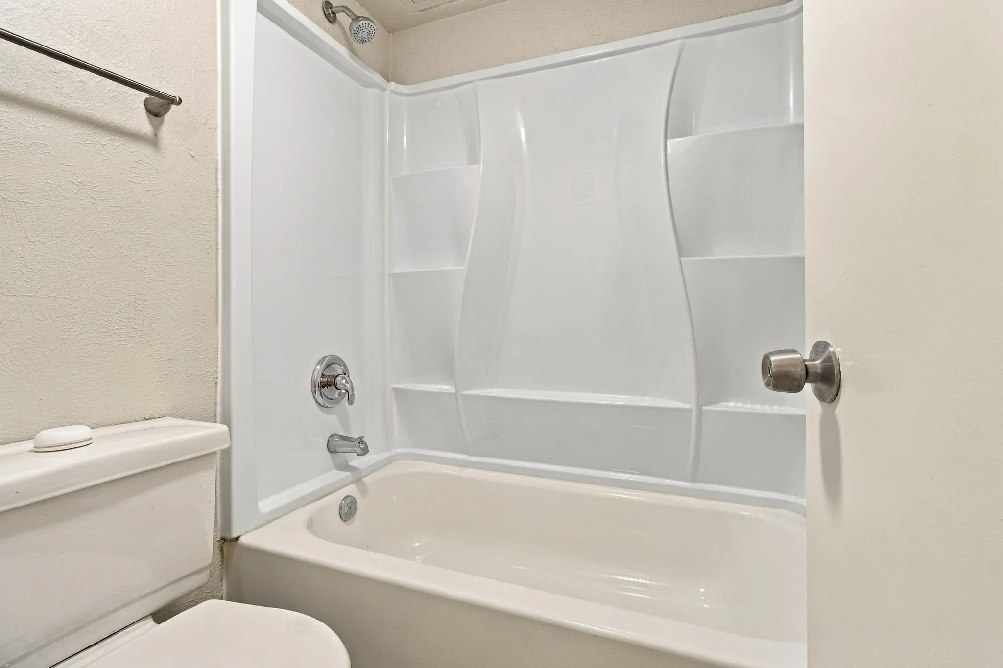 White acrylic tub and shower combination with chrome fixtures and integrated shelving