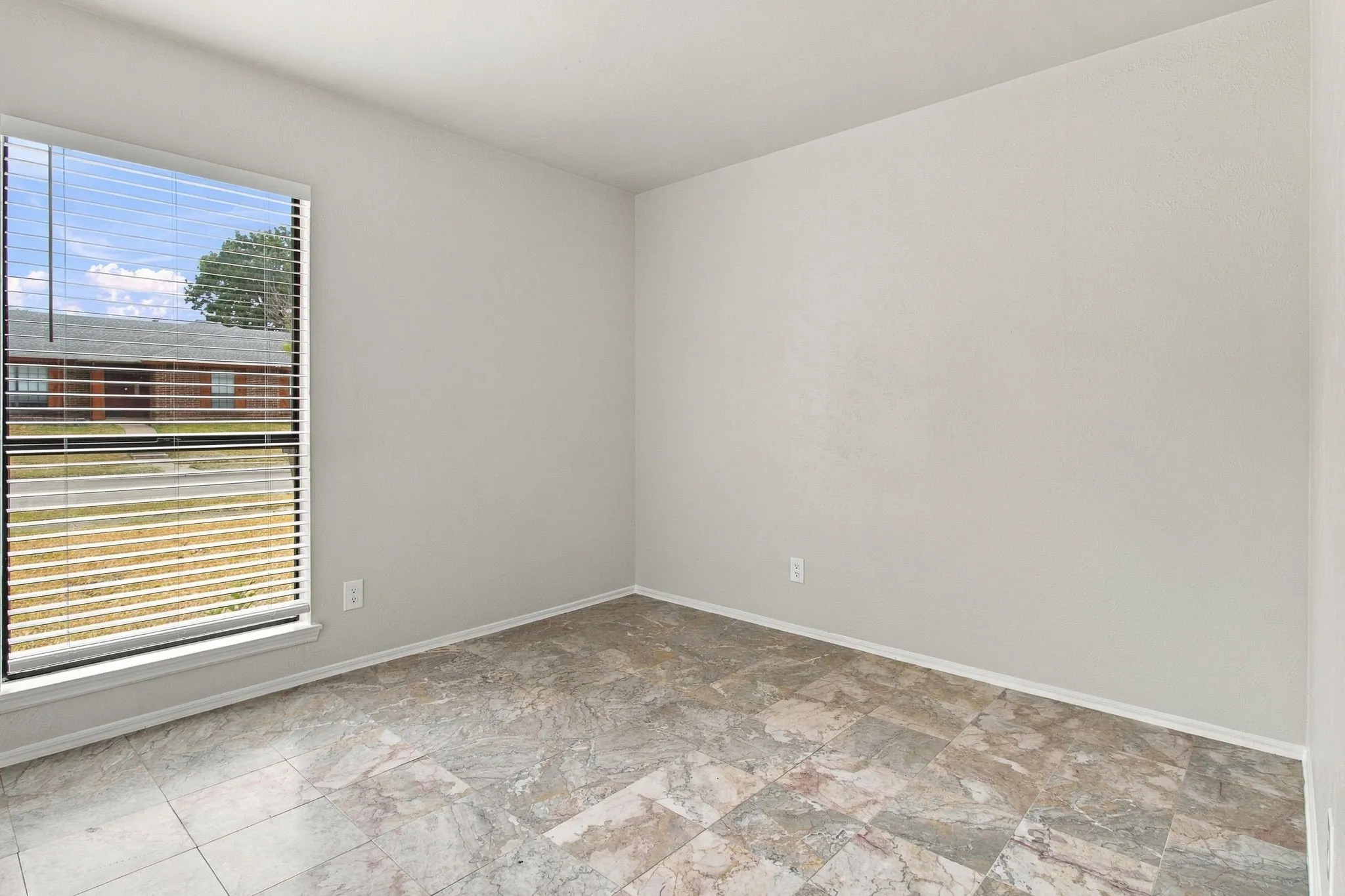 Light gray walls with a textured finish, a window featuring horizontal blinds, and multi-toned tile flooring