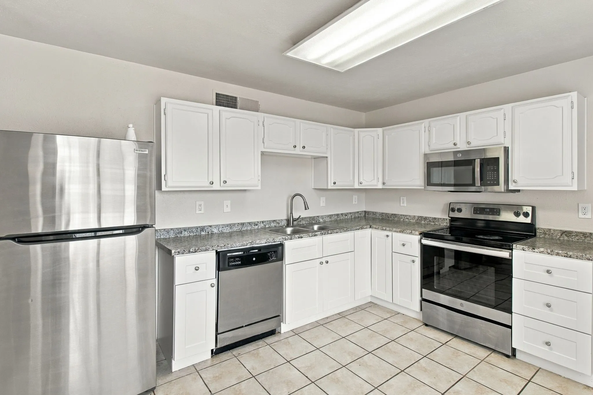 Kitchen featuring white cabinetry, granite-style countertops, stainless steel appliances, and tiled flooring