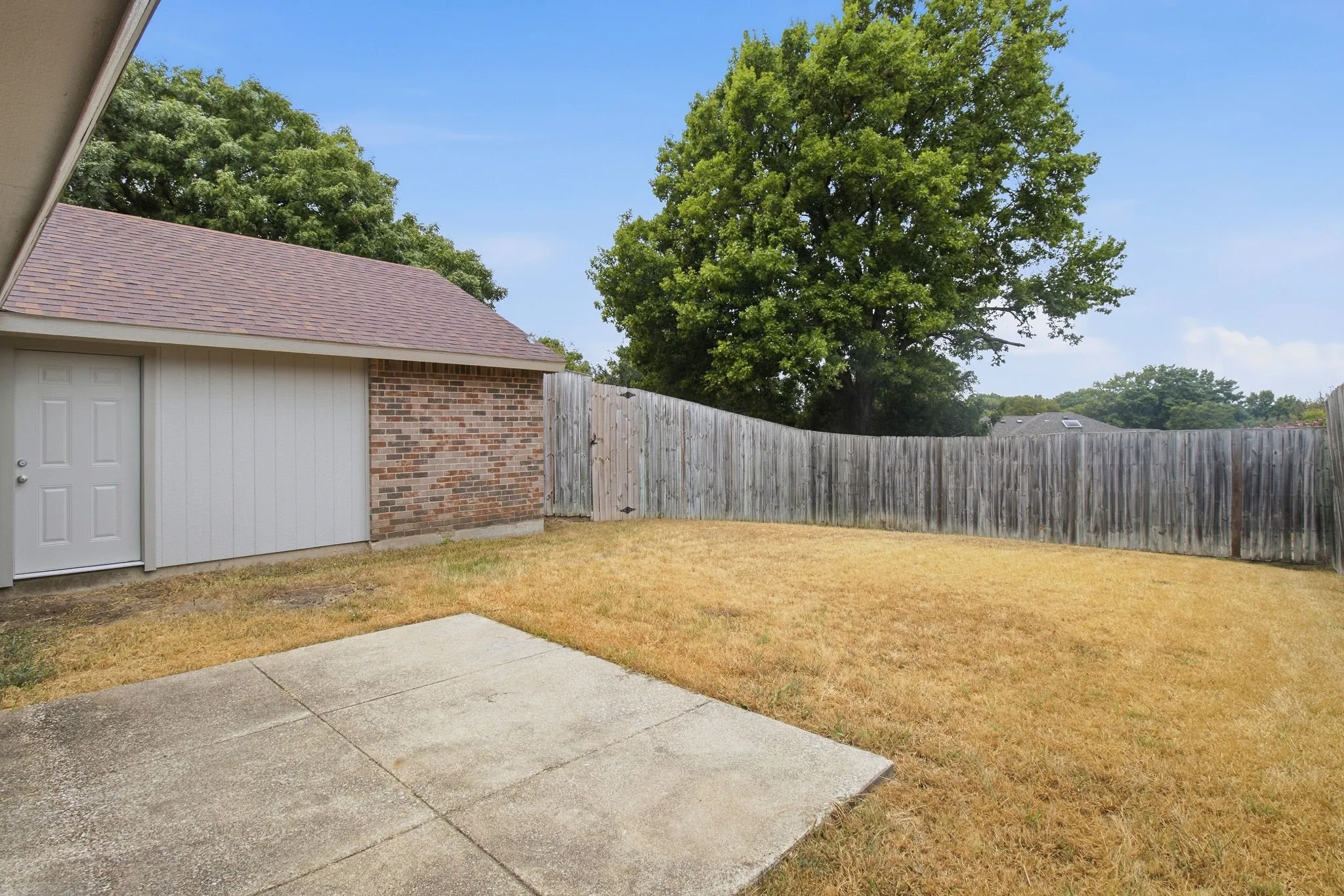 Detached brick and siding structure with a shingle roof, concrete patio, and wood privacy fencing