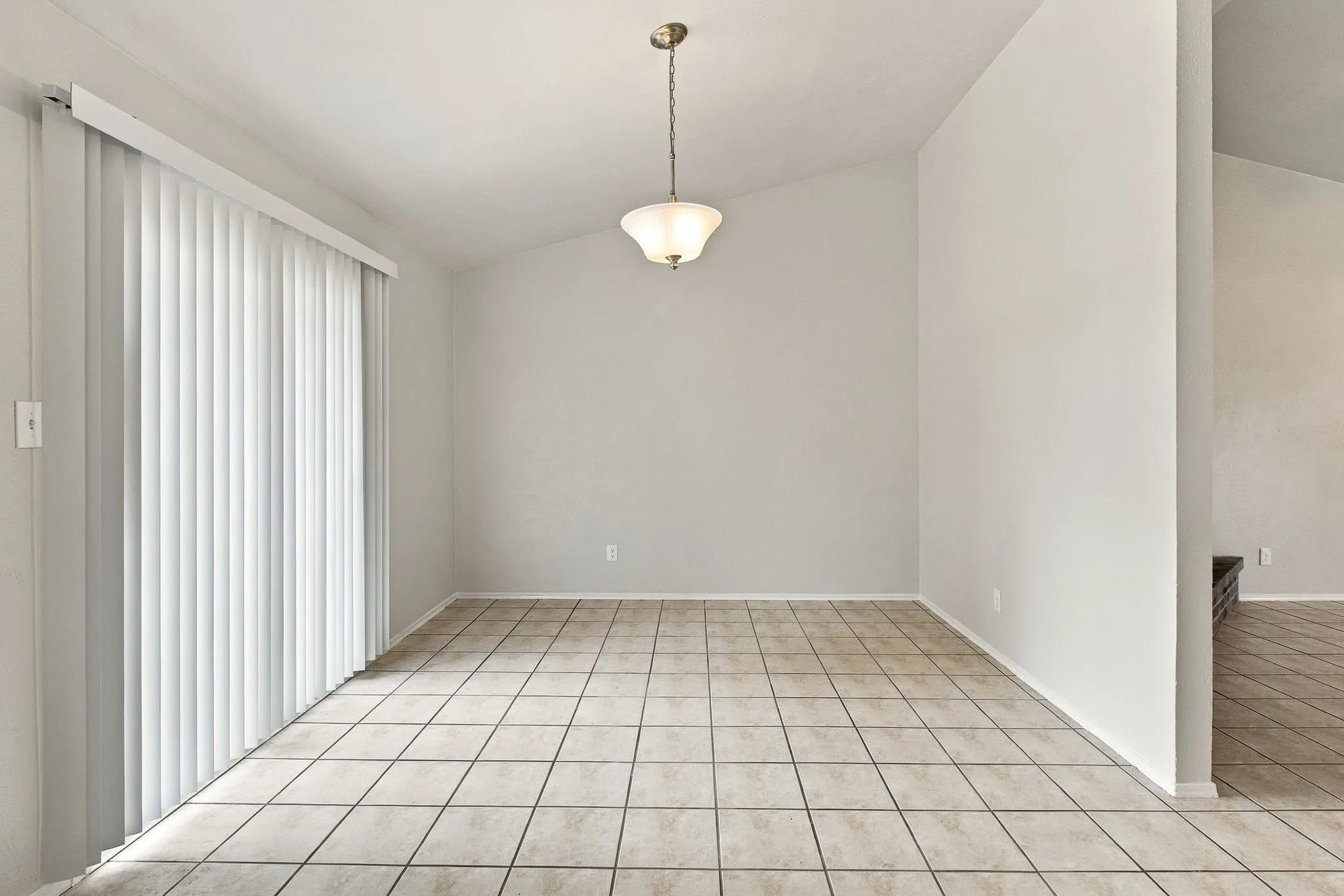 Spacious room featuring vaulted ceilings, a suspended light fixture, tiled flooring, and a sliding glass door with vertical​​‌​​​​‌​​‌‌​‌‌​​​‌‌​‌​‌​‌​​​‌​​ blinds
