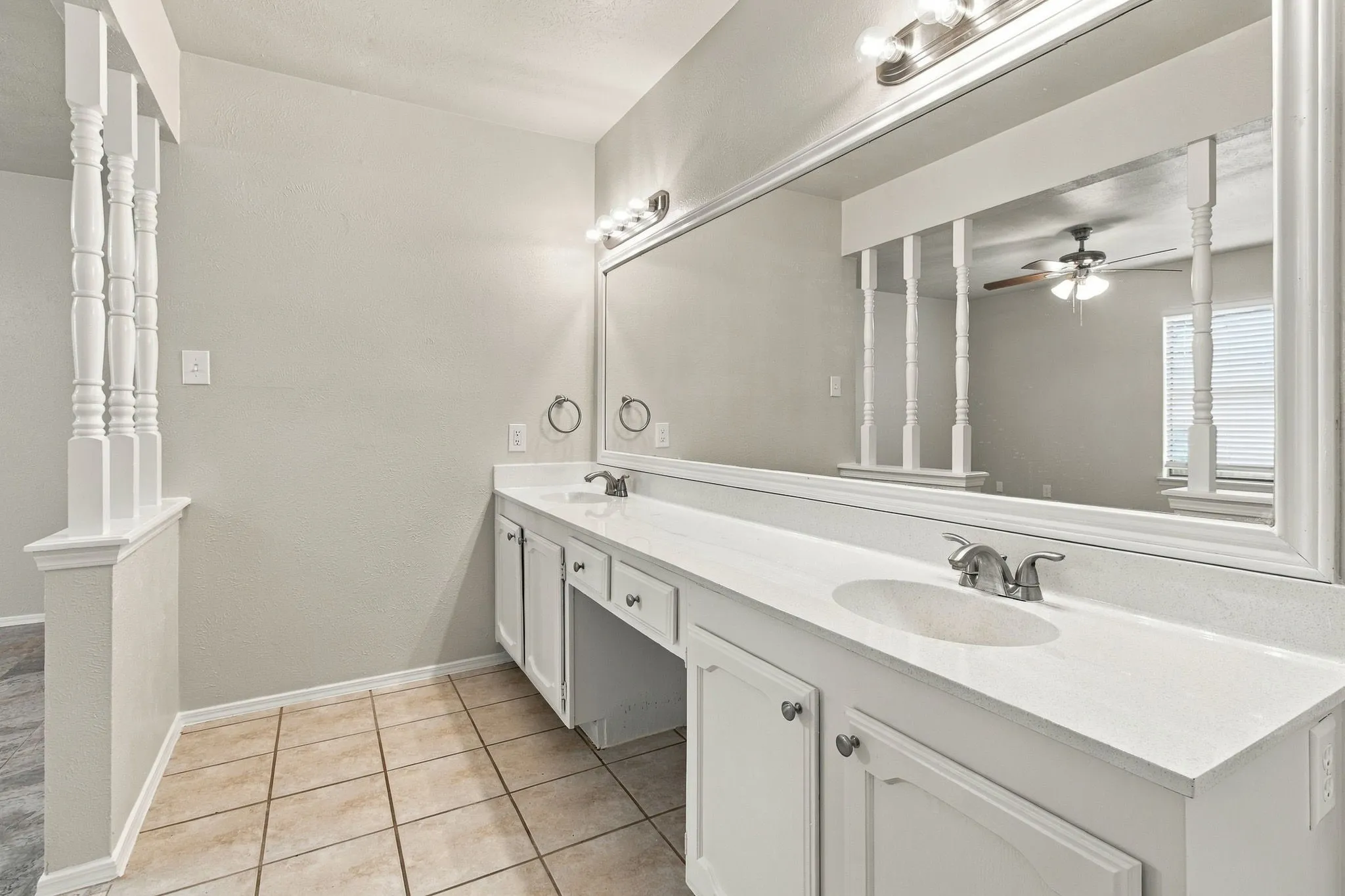 Double vanity with integrated sinks, white cabinetry, chrome fixtures, and a large wall-mounted mirror