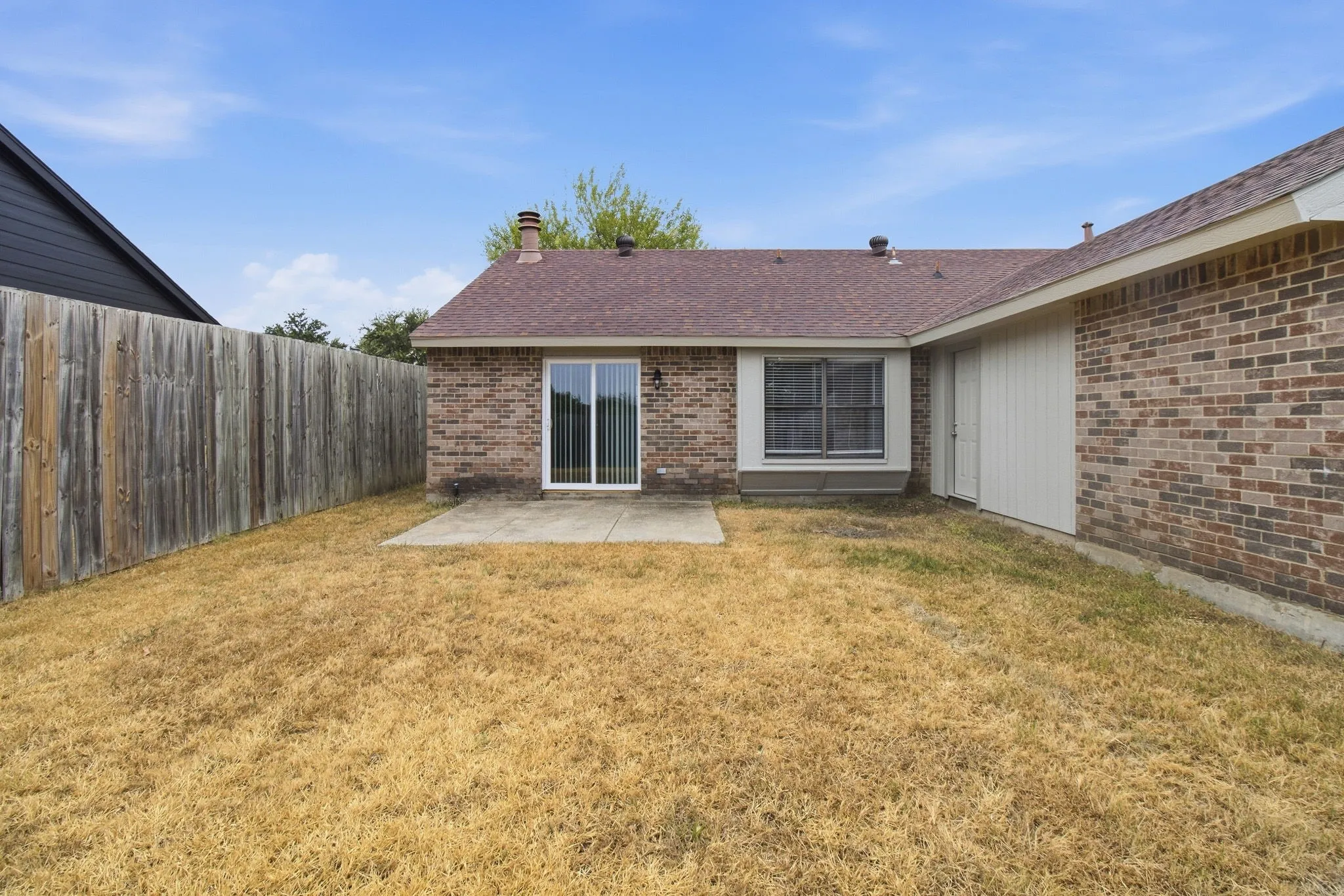 Private backyard featuring a concrete patio, wood privacy fence, and brick exterior