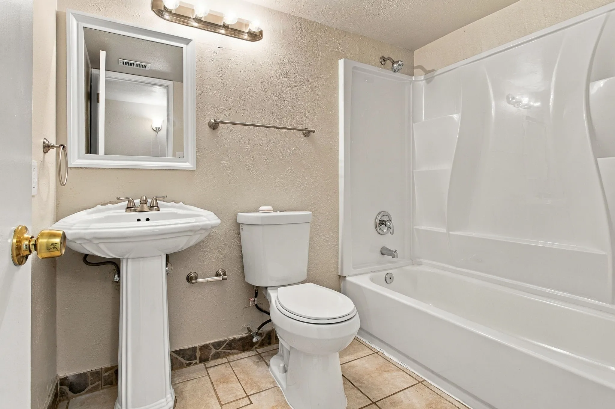 Pedestal sink with dual-handle faucet, toilet, and a combined tub and shower unit with a white surround