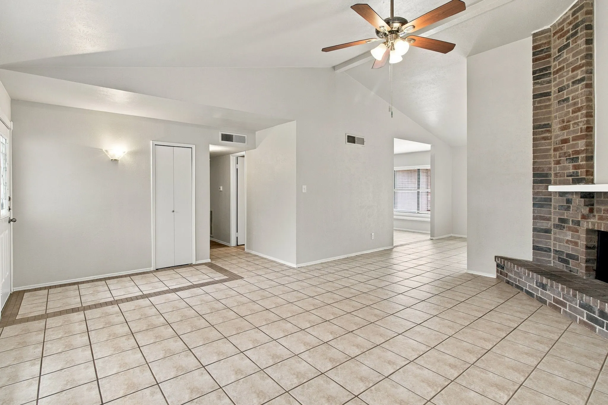 Vaulted ceiling with a ceiling fan, brick fireplace, tile flooring, and wall sconce lighting
