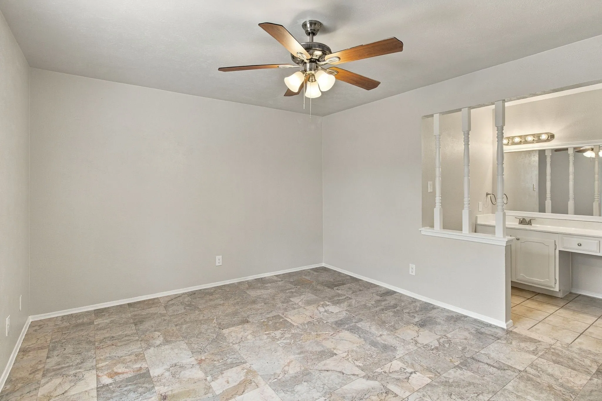 Textured tile flooring, ceiling fan with integrated lighting, and a half-wall with decorative spindles