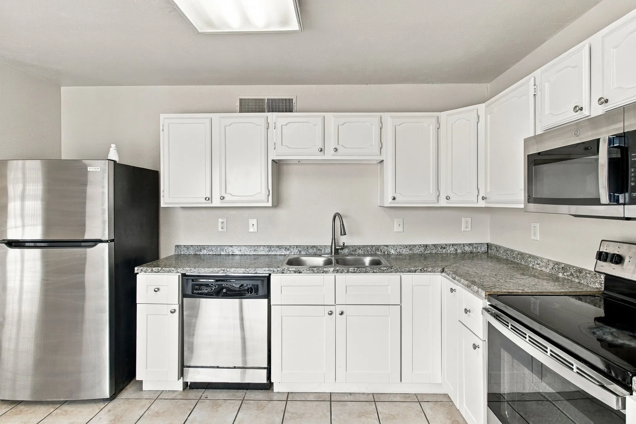 White cabinetry, granite-patterned countertops, stainless steel appliances, dual basin sink, and tile flooring