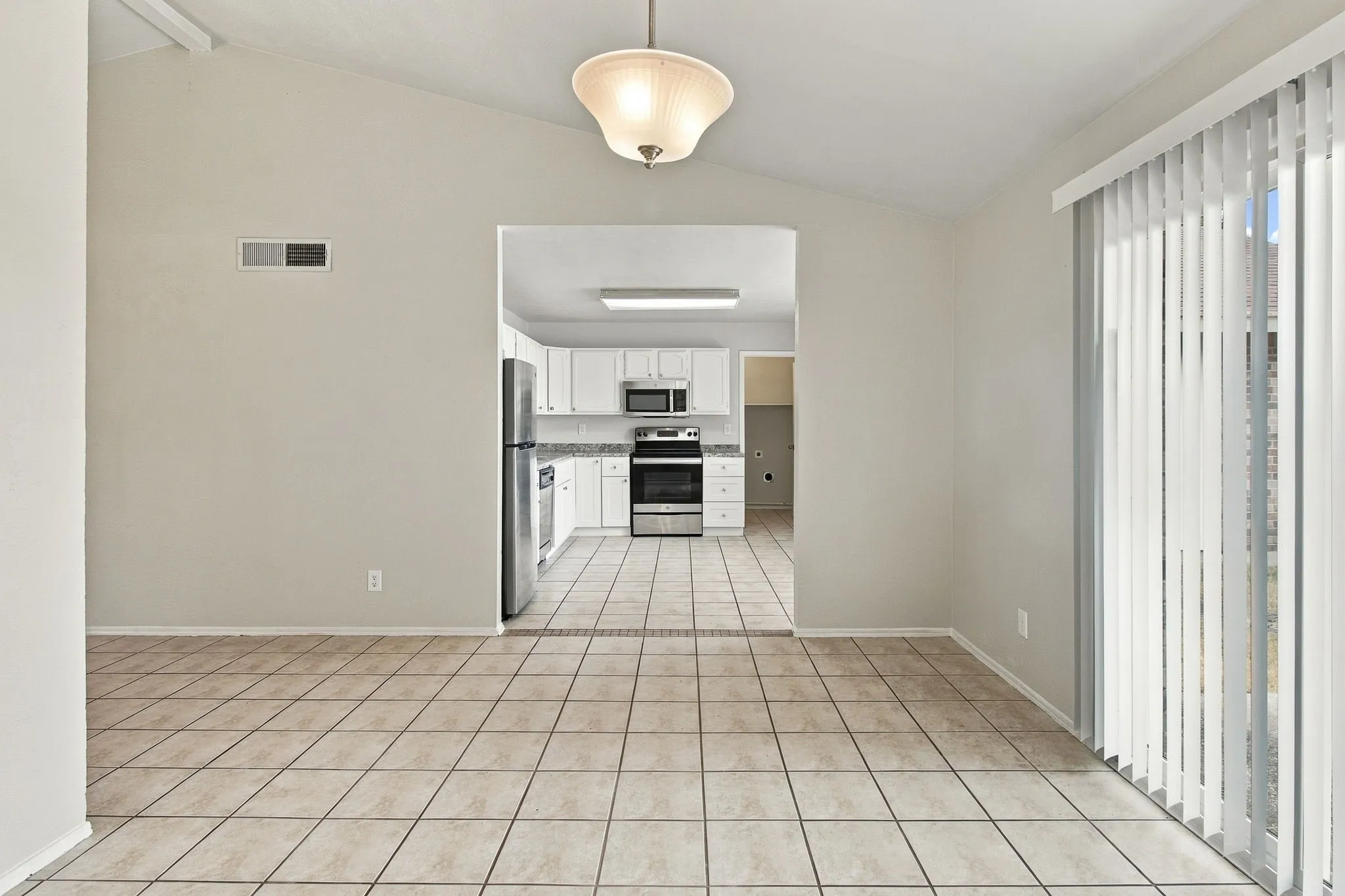 Vaulted ceiling with a flush mount light fixture, tile flooring, and vertical blinds on the glass door