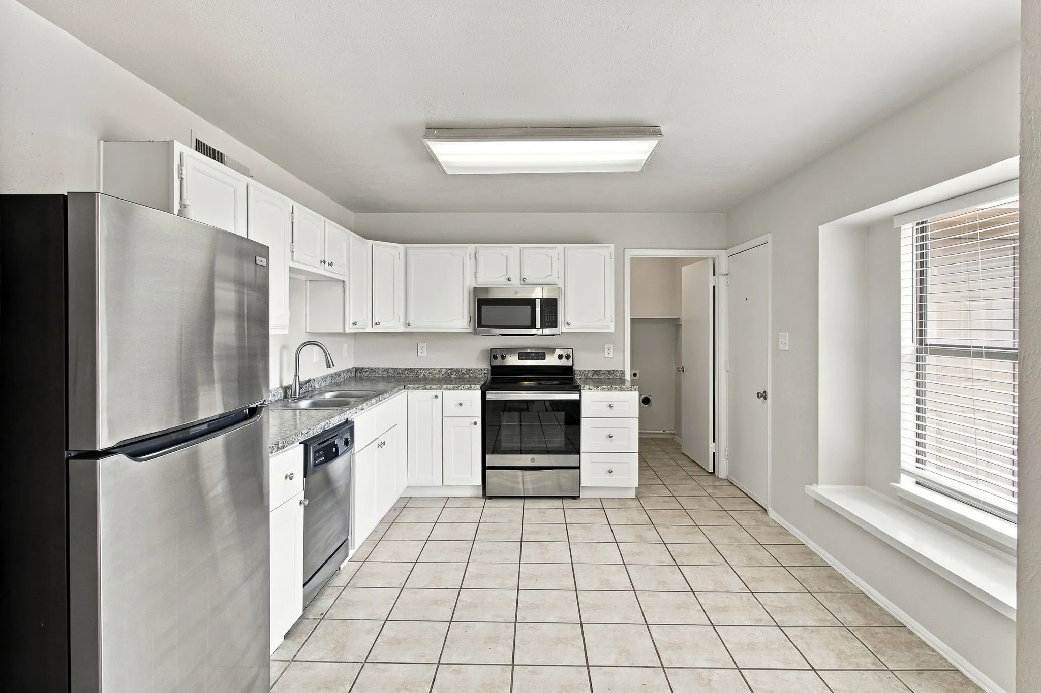 Kitchen featuring white cabinetry, stainless steel appliances, granite-look countertops, and tile flooring