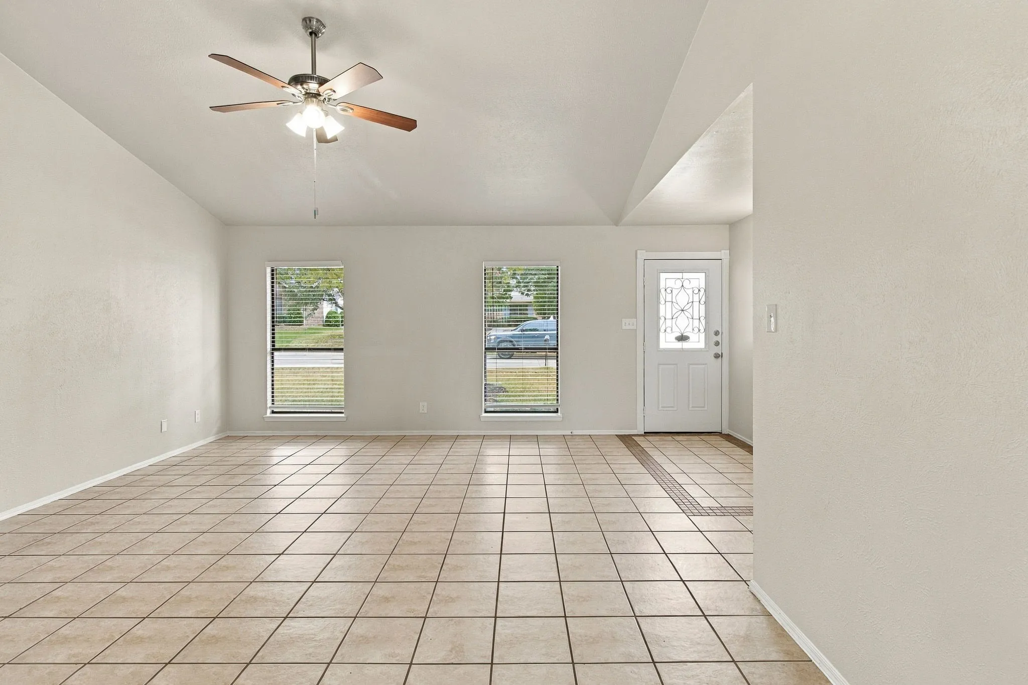 Vaulted ceiling with a ceiling fan, tiled flooring, two windows with blinds, and a paneled front door with decorative glass