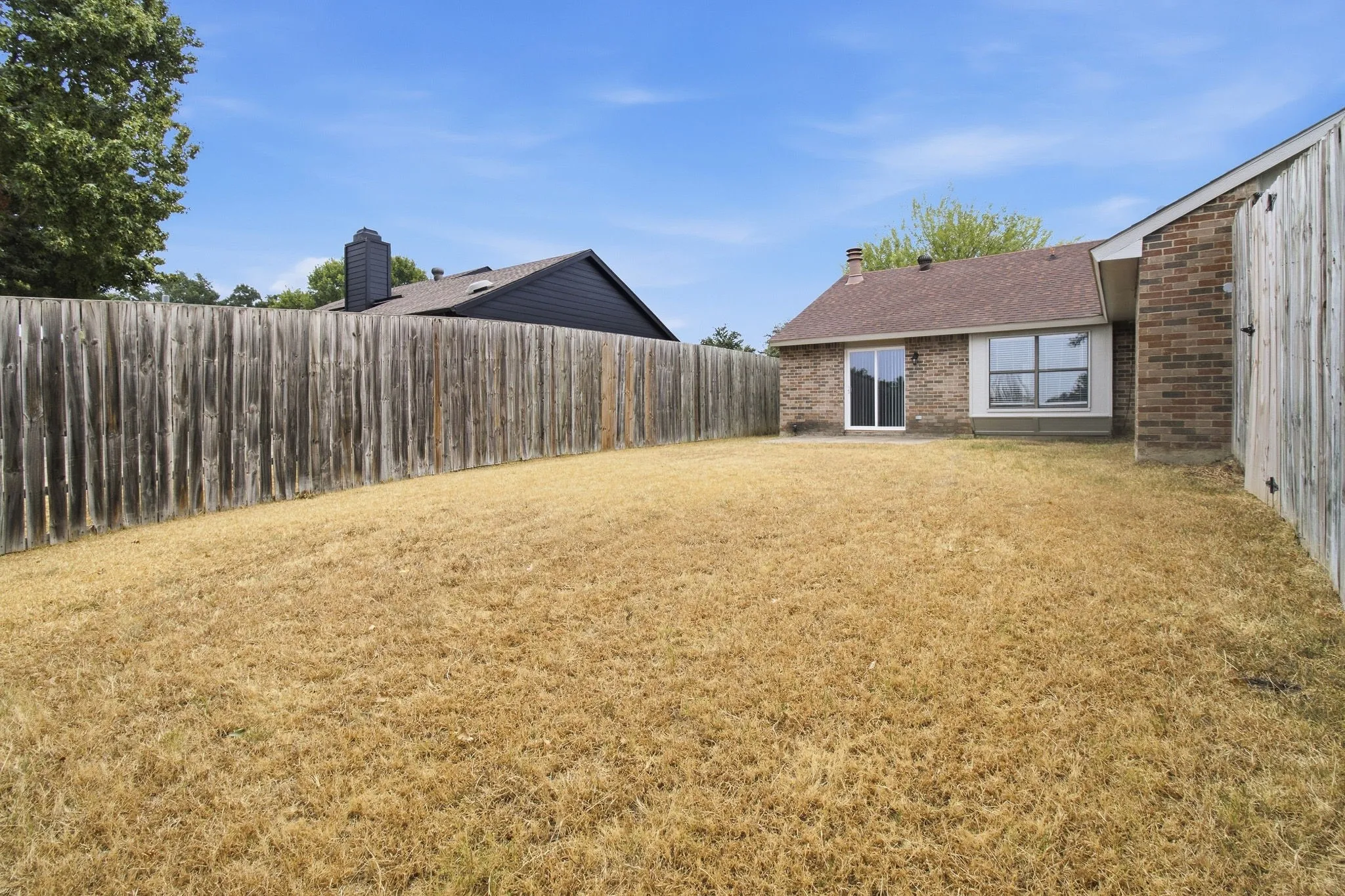 Expansive backyard with a full privacy fence, brick exterior, and a sliding glass door