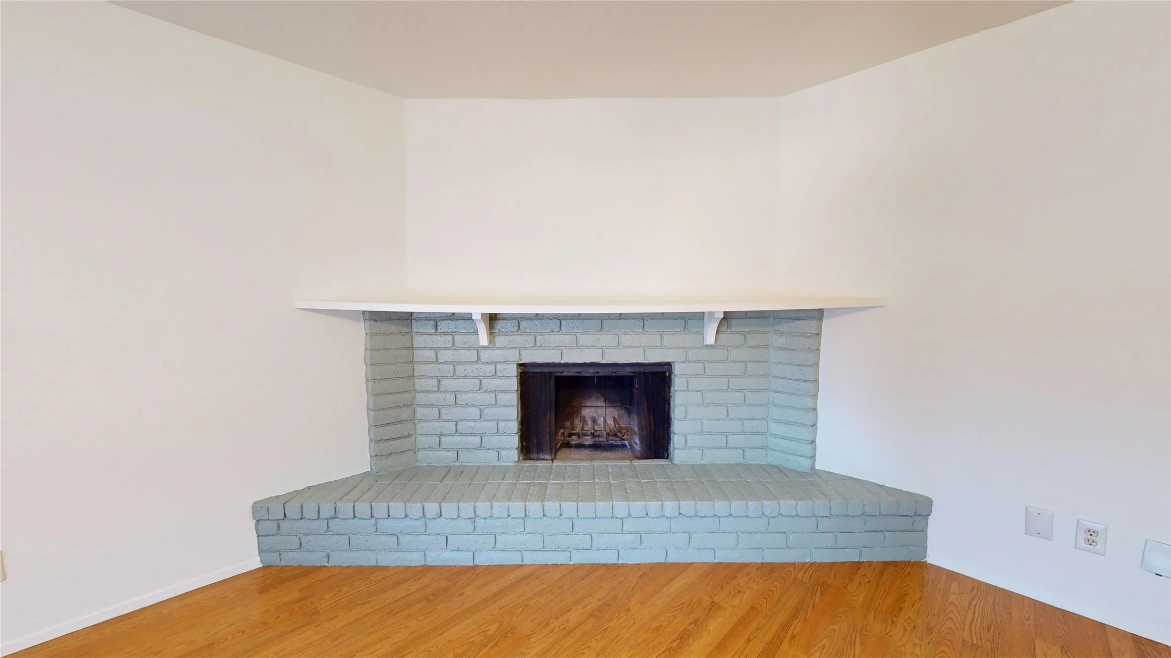 Corner-positioned brick fireplace with a painted finish, mantel, and wood-finish flooring