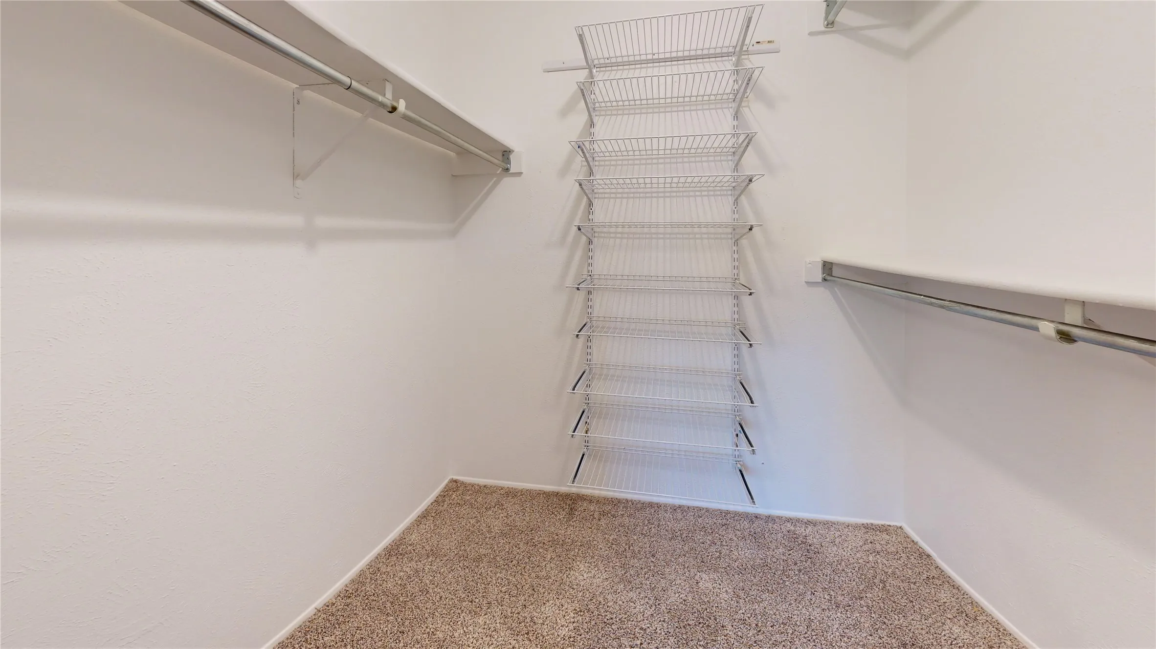 Built-in wire shelving, wire hanging rods, and light-toned carpet flooring