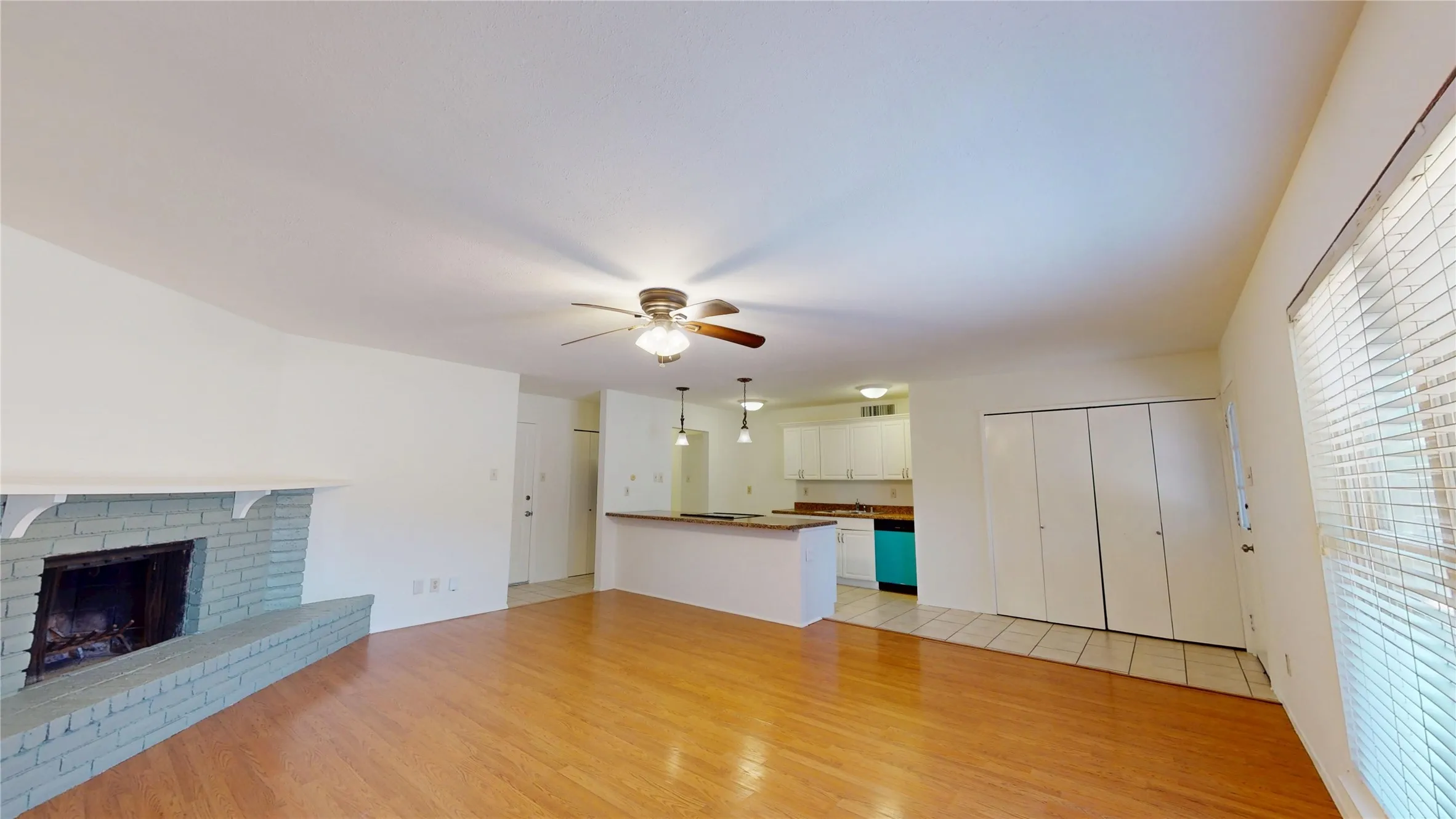 Wood-finish flooring with a brick fireplace, ceiling fan, and white walls