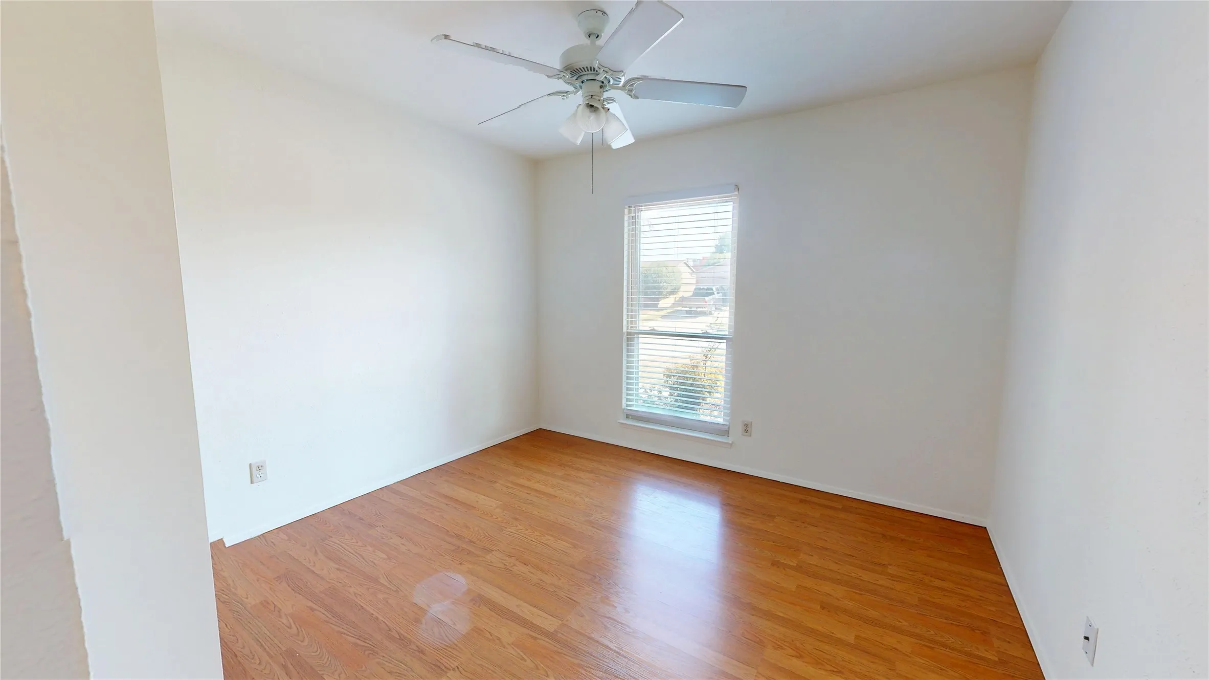 Hardwood flooring, crisp white walls, and a window with horizontal blinds