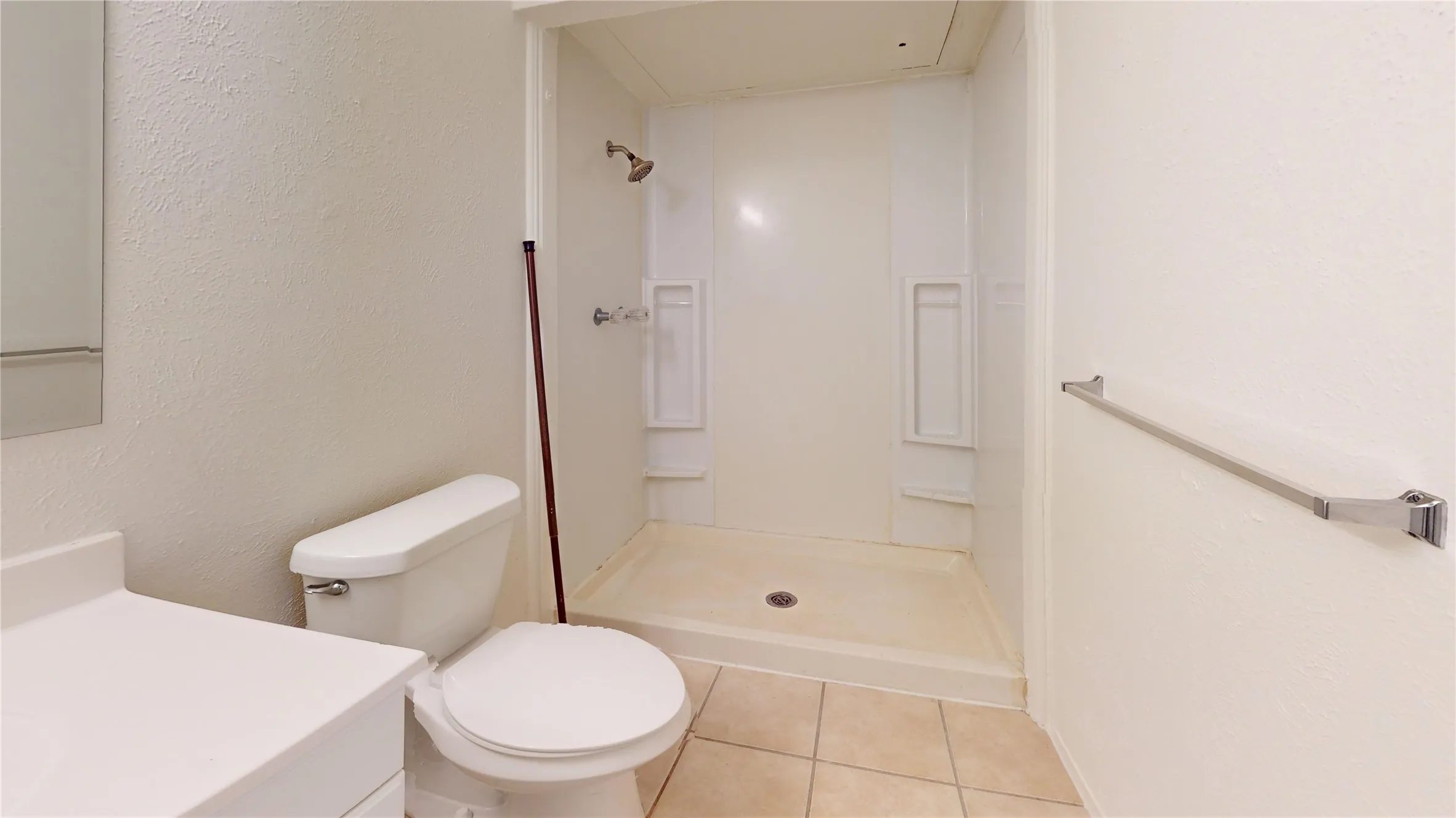 Shower with integrated shelving, tile flooring, vanity with a solid surface countertop, and a toilet