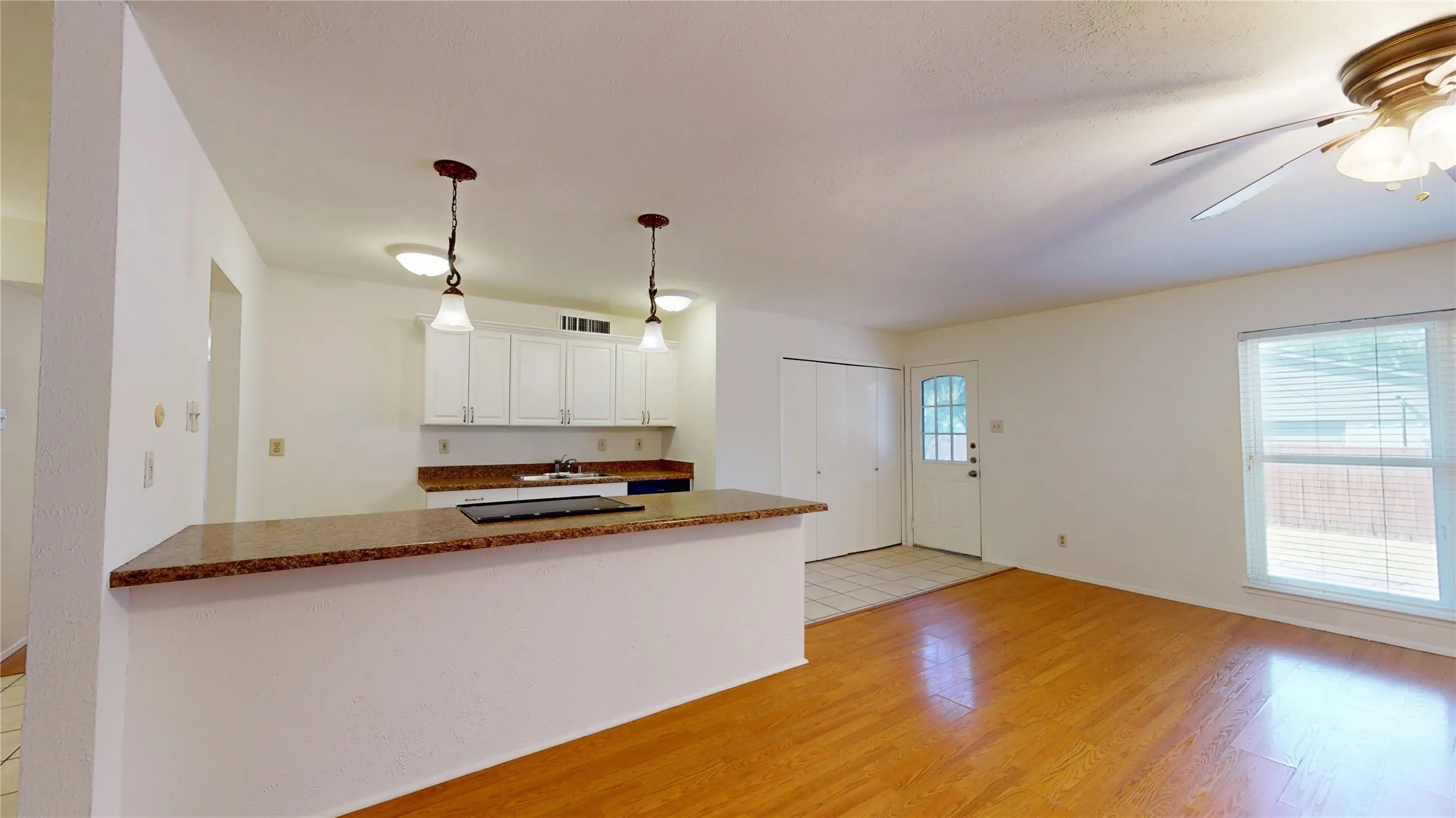 Wood-finish flooring, white cabinetry, granite-patterned countertop, and ceiling fan with integrated lighting
