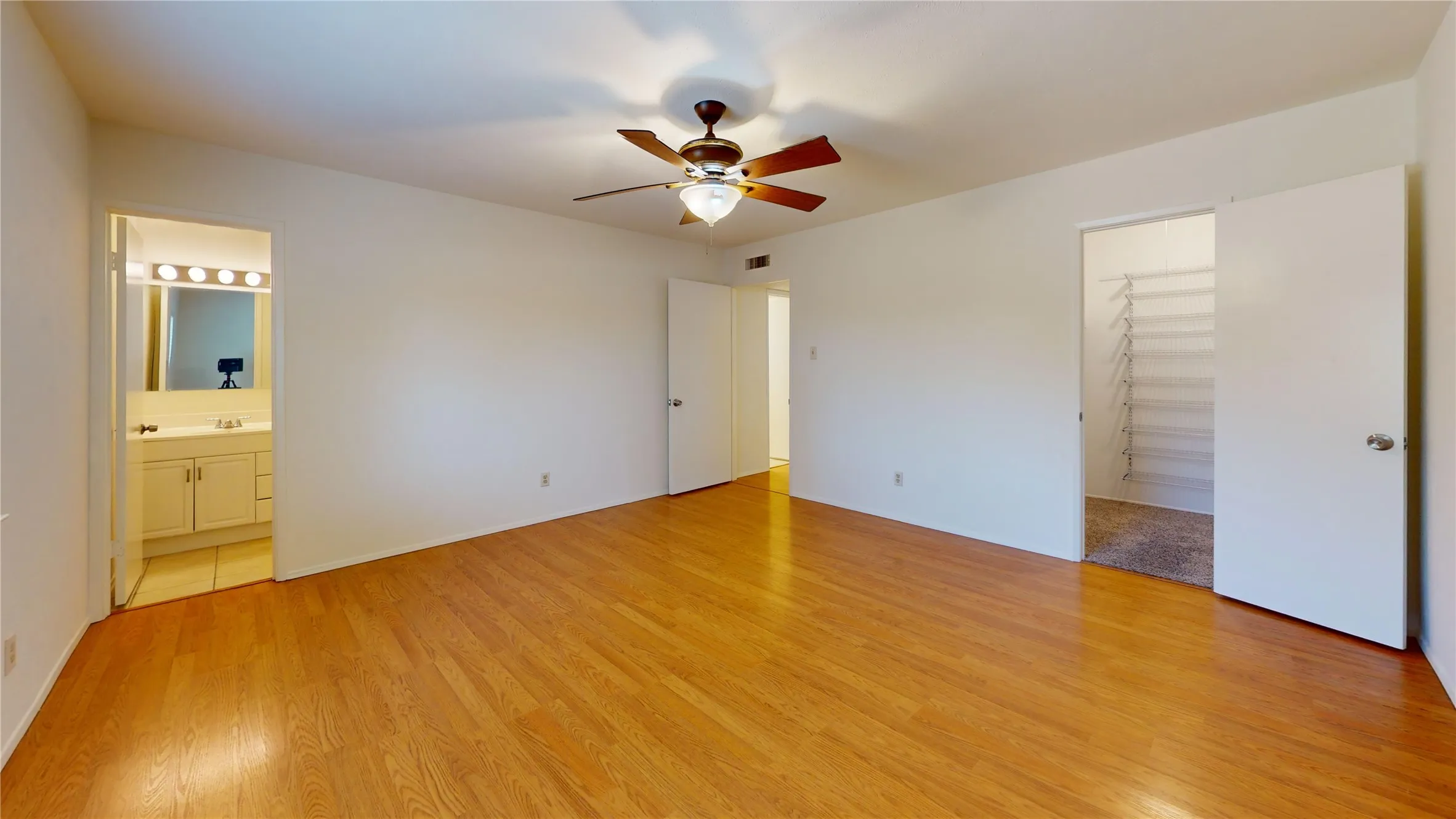 Wood-finish flooring throughout, with a ceiling fan light fixture, an integrated bathroom vanity, and a wire shelving closet system