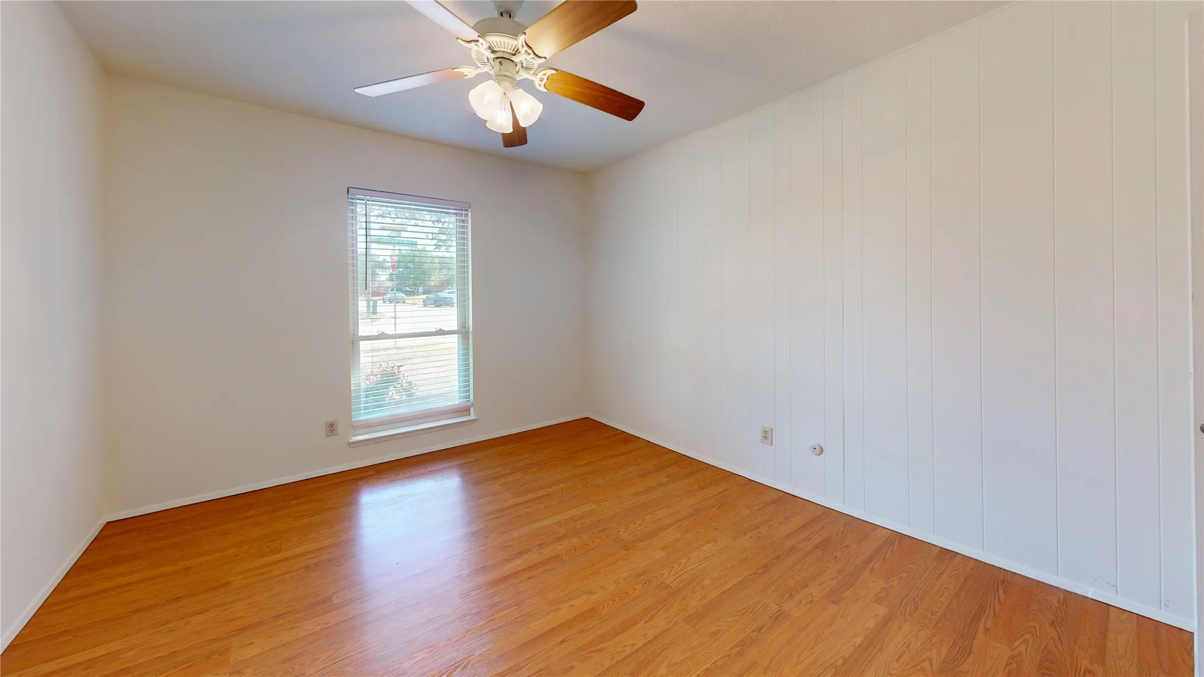 Wood-finish flooring, white paneled wall, ceiling fan with light fixture, and window with blinds