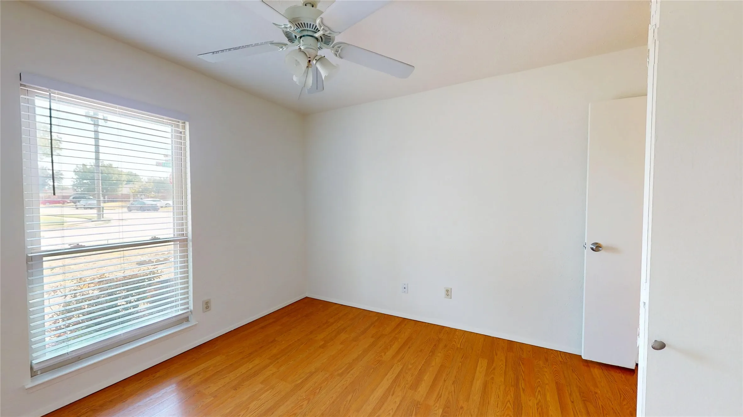 Hardwood-style flooring, a large window with blinds, a ceiling fan with light fixture, and white painted walls