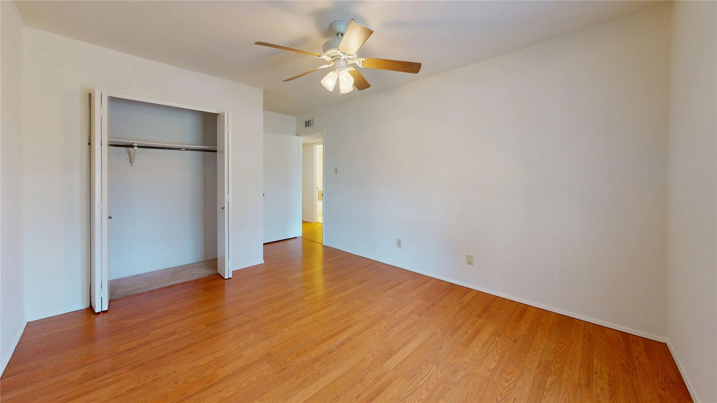Wood-finish flooring with a ceiling fan, bifold closet doors, and a white wall finish