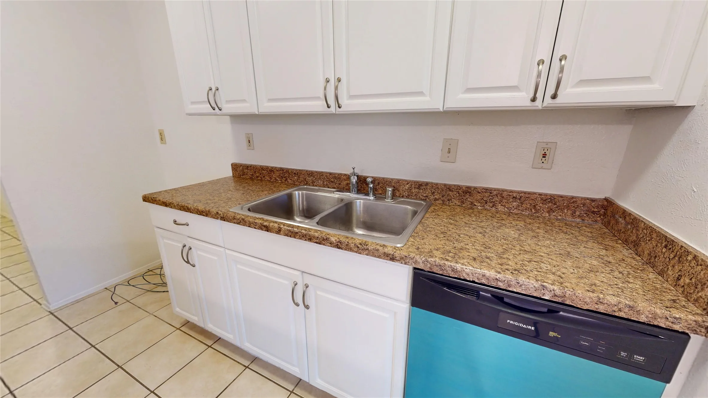 White cabinetry with brushed nickel hardware, speckled brown countertop, double basin stainless steel sink, and a built-in dishwasher
