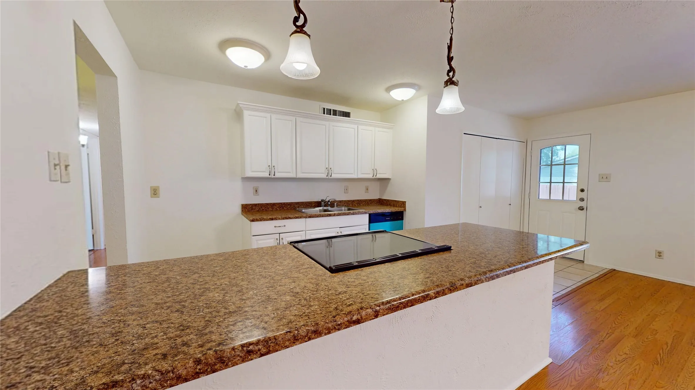 Kitchen featuring white cabinetry, speckled countertops, a built-in cooktop, and two pendant lights