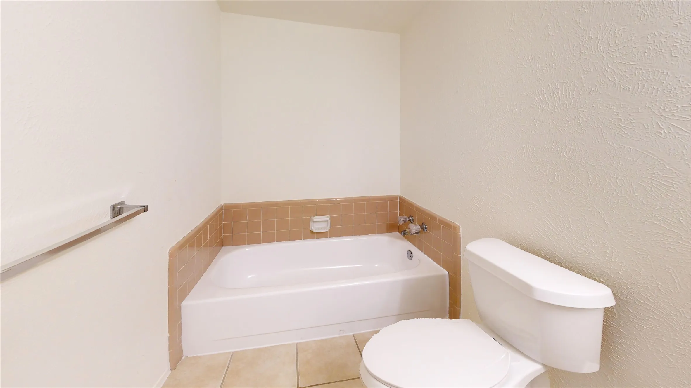 Corner soaking tub with tiled surround, white porcelain toilet, and light-toned floor tiling