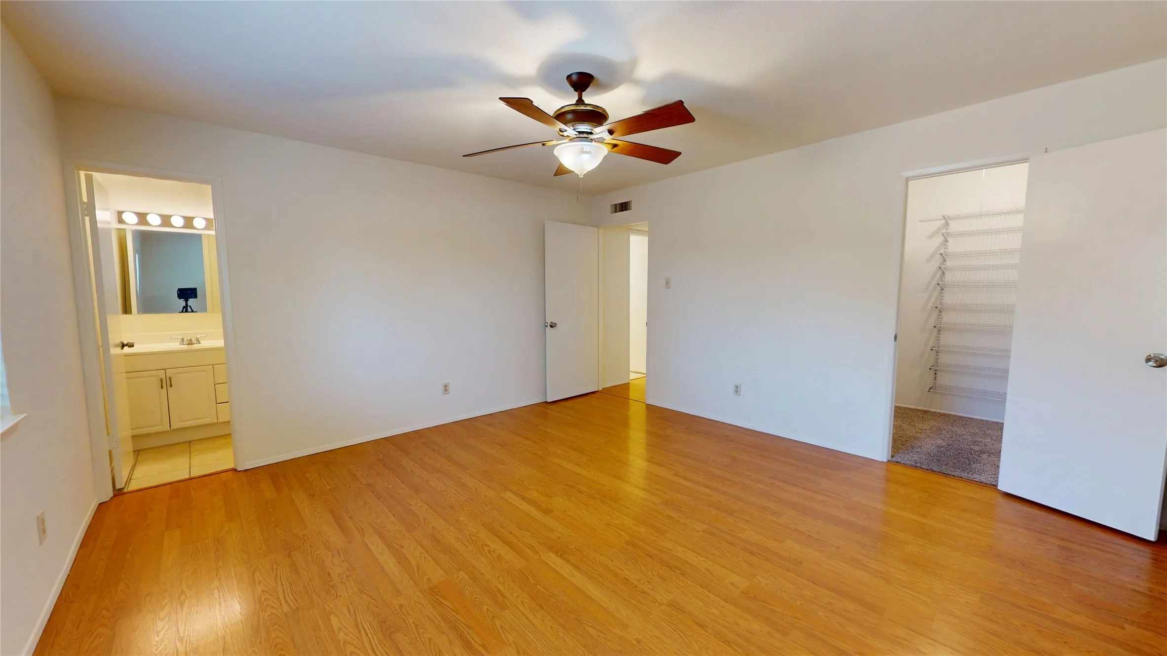 Spacious room with wood-finish flooring, ceiling fan, and built-in closet shelving