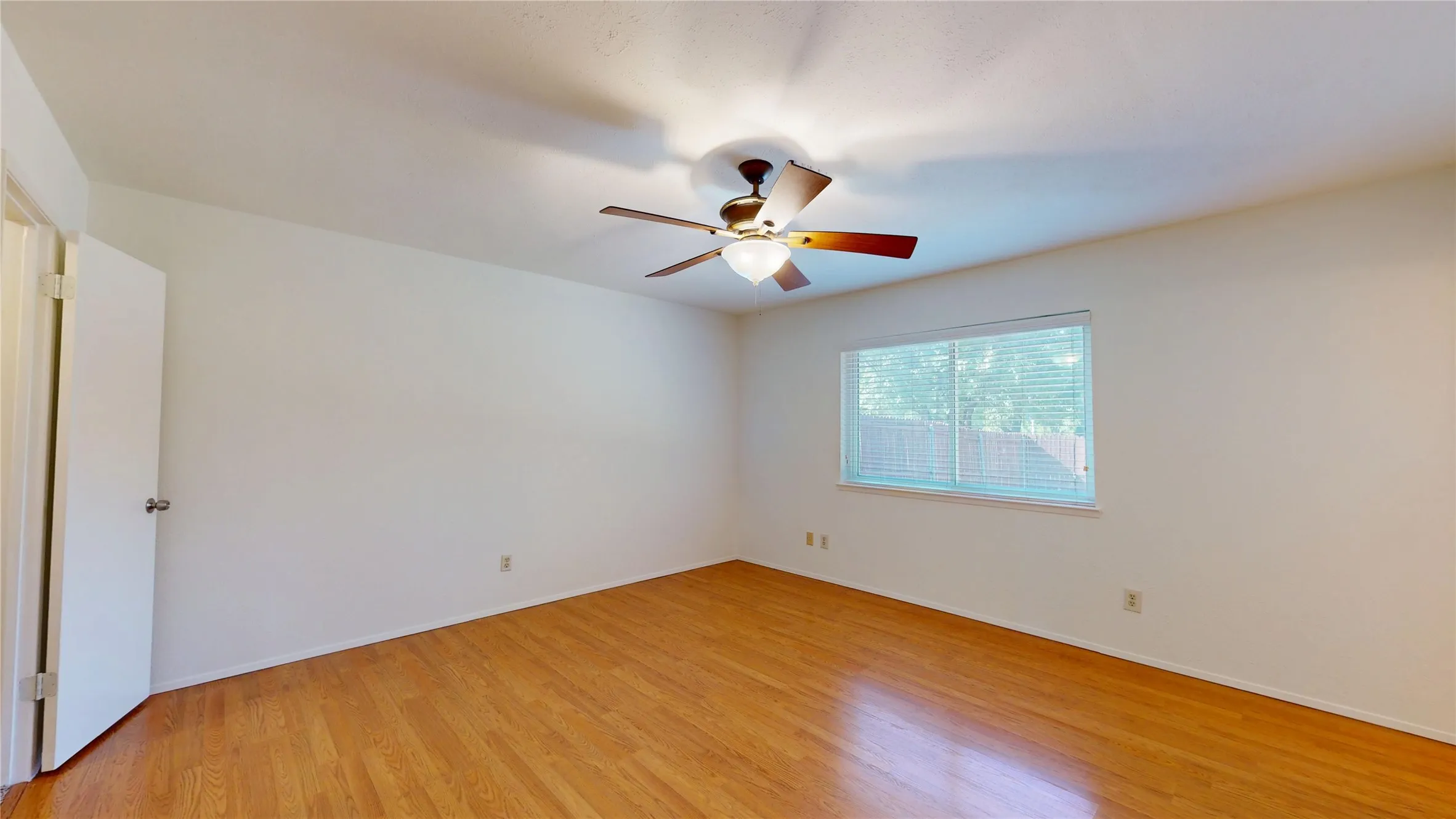 Wood-finish flooring throughout, bright white walls, and a window with horizontal blinds