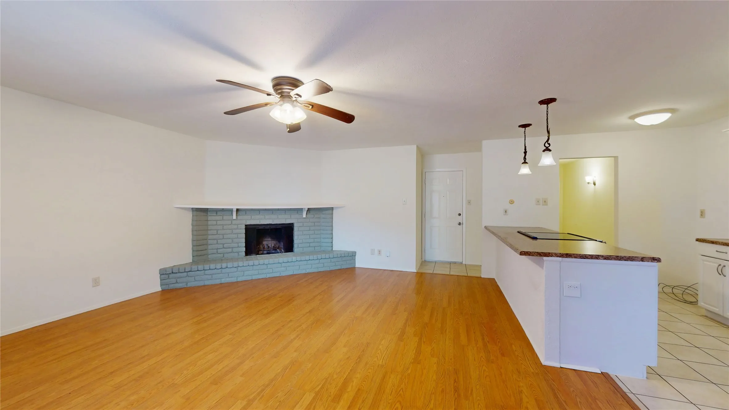 Wood-finish flooring, brick fireplace with mantel, ceiling fan with integrated lighting, kitchen island with built-in cooktop, and pendant lighting