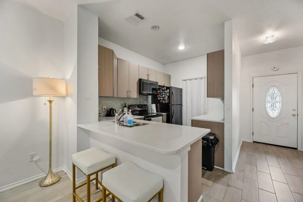 Compact kitchen featuring light-toned cabinetry, a white countertop with a breakfast bar, and stainless steel appliances