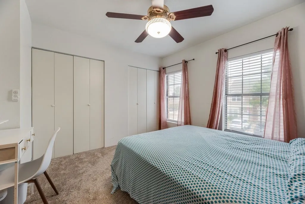 Carpeted room featuring dual windows with blinds, bi-fold closet doors, and a ceiling fan with integrated lighting