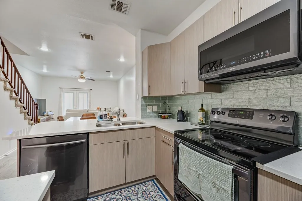 Contemporary kitchen featuring light wood-finish cabinetry, light-toned countertops, a full suite of black appliances, and a subway tile backsplash