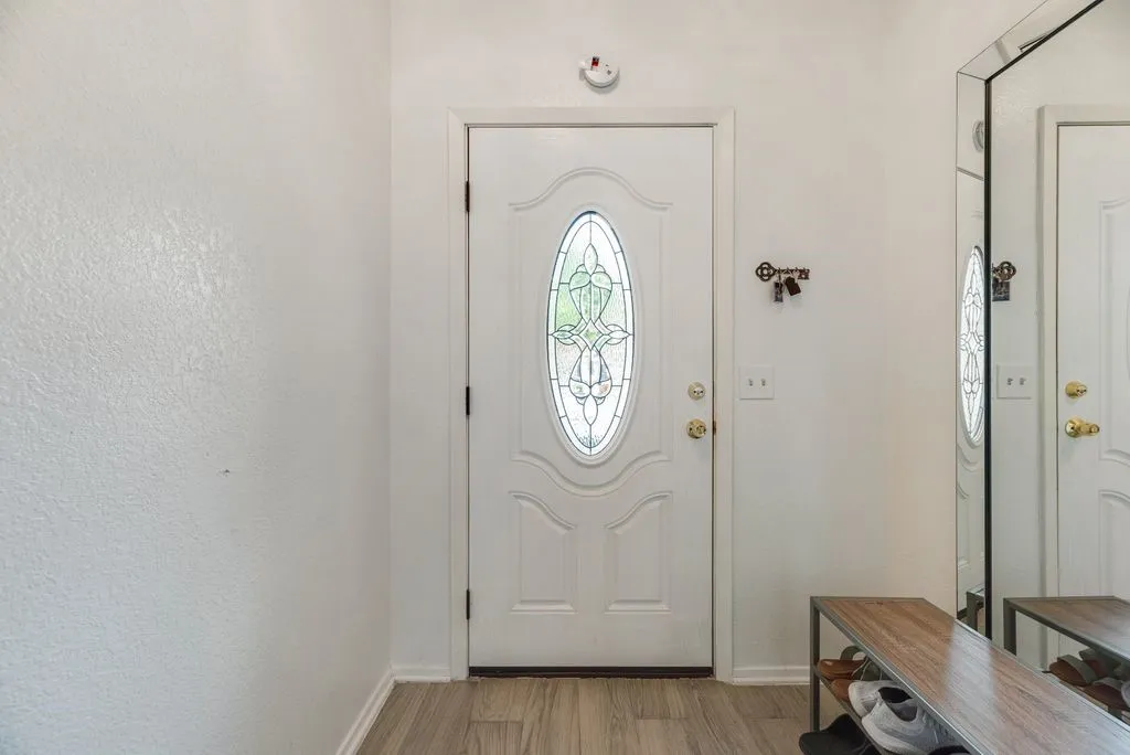 Entry door with decorative oval glass insert, wood-finish flooring, and white trim