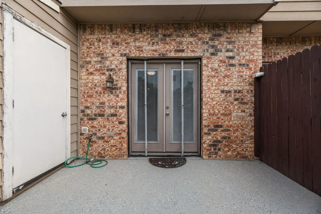 Brick wall exterior featuring double entry doors, an outdoor light fixture, and a privacy fence