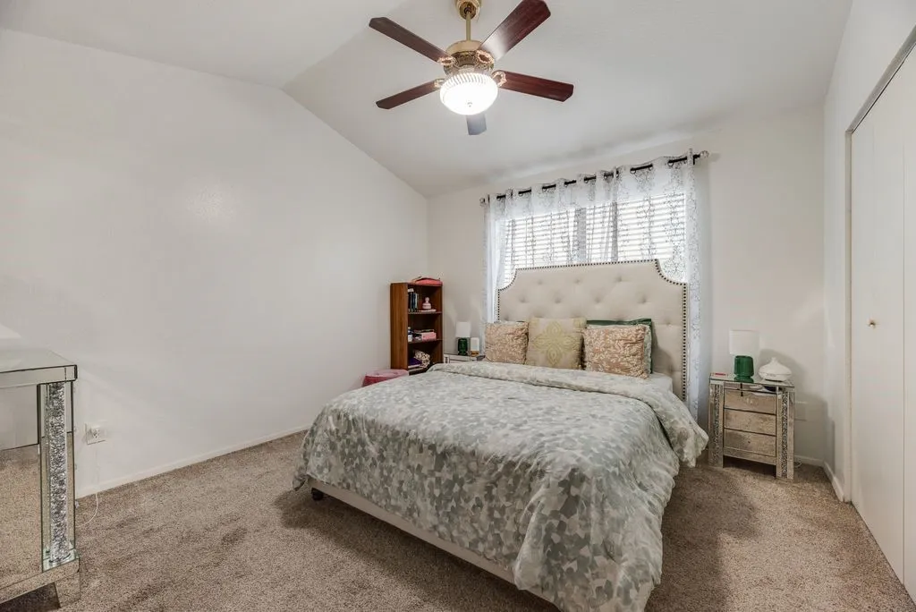 Vaulted ceiling with a ceiling fan, carpet flooring, and a built-in closet with bifold doors