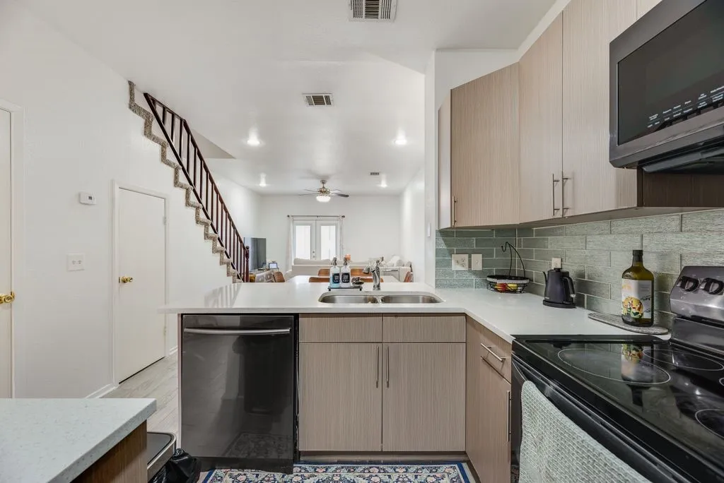 Modern kitchen featuring light wood-finish cabinetry, stainless steel appliances, white subway tile backsplash, and quartz countertops