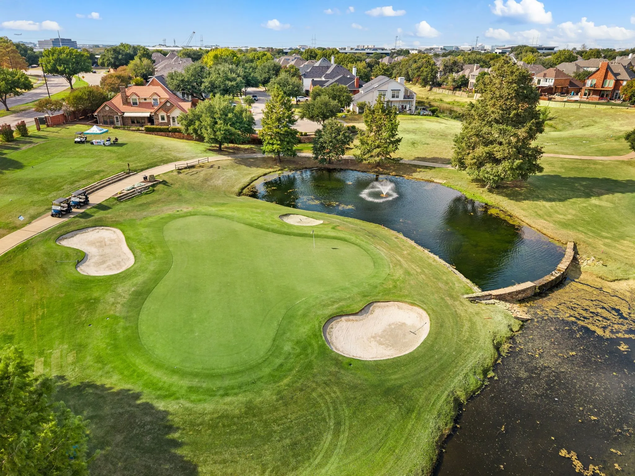 Expansive golf course featuring a manicured green, sand bunkers, and a water hazard with a fountain