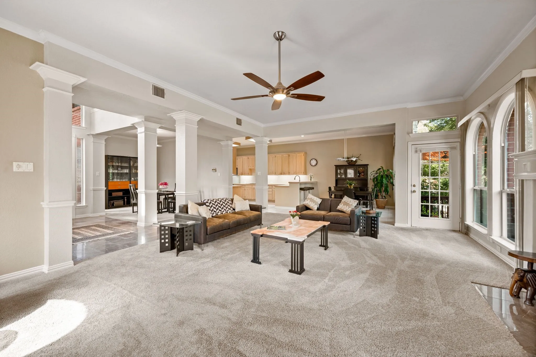 Spacious living area featuring carpet flooring, column architectural details, a ceiling fan, and multiple arched windows