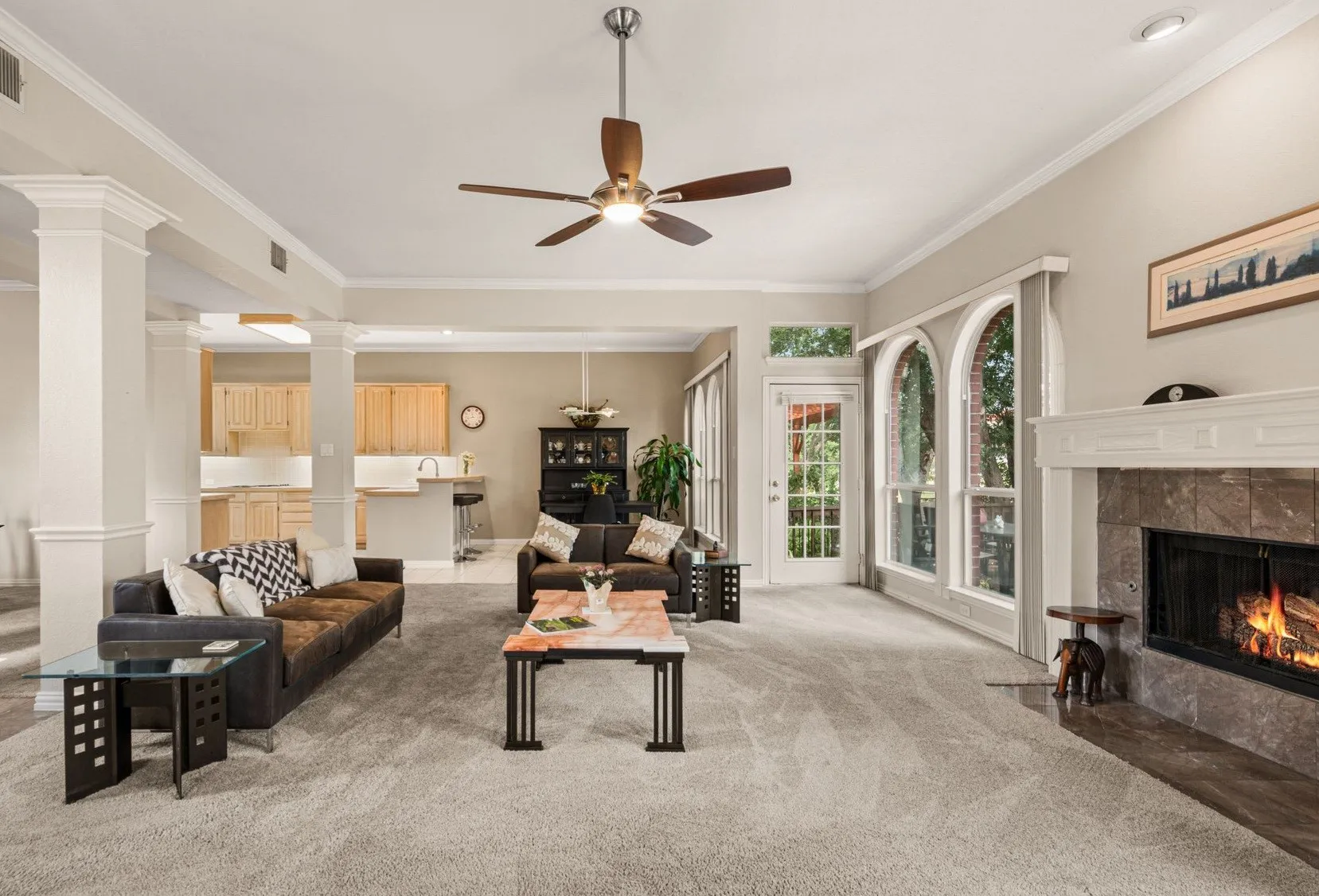 Spacious living area featuring a stone fireplace with a substantial mantel, arched windows, and a ceiling fan