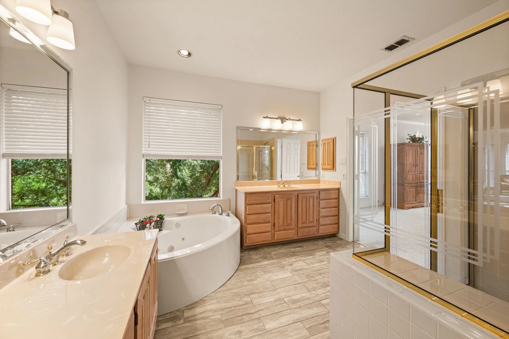 Dual vanity with integrated sinks, corner jetted tub, wood-finish flooring, and a glass-enclosed shower